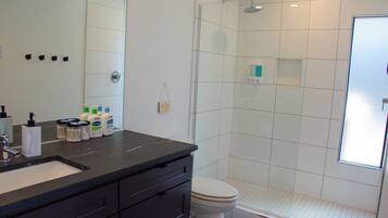 A modern bathroom with a black countertop, white tiles, a glass-enclosed shower, and a toilet.