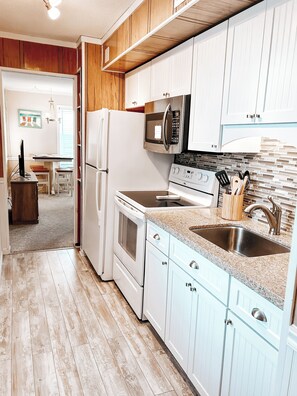 A kitchen with white cabinets, a granite countertop, a microwave, a stove, and a sink. - Wake Up to the Sound of Waves (North Myrtle Beach)