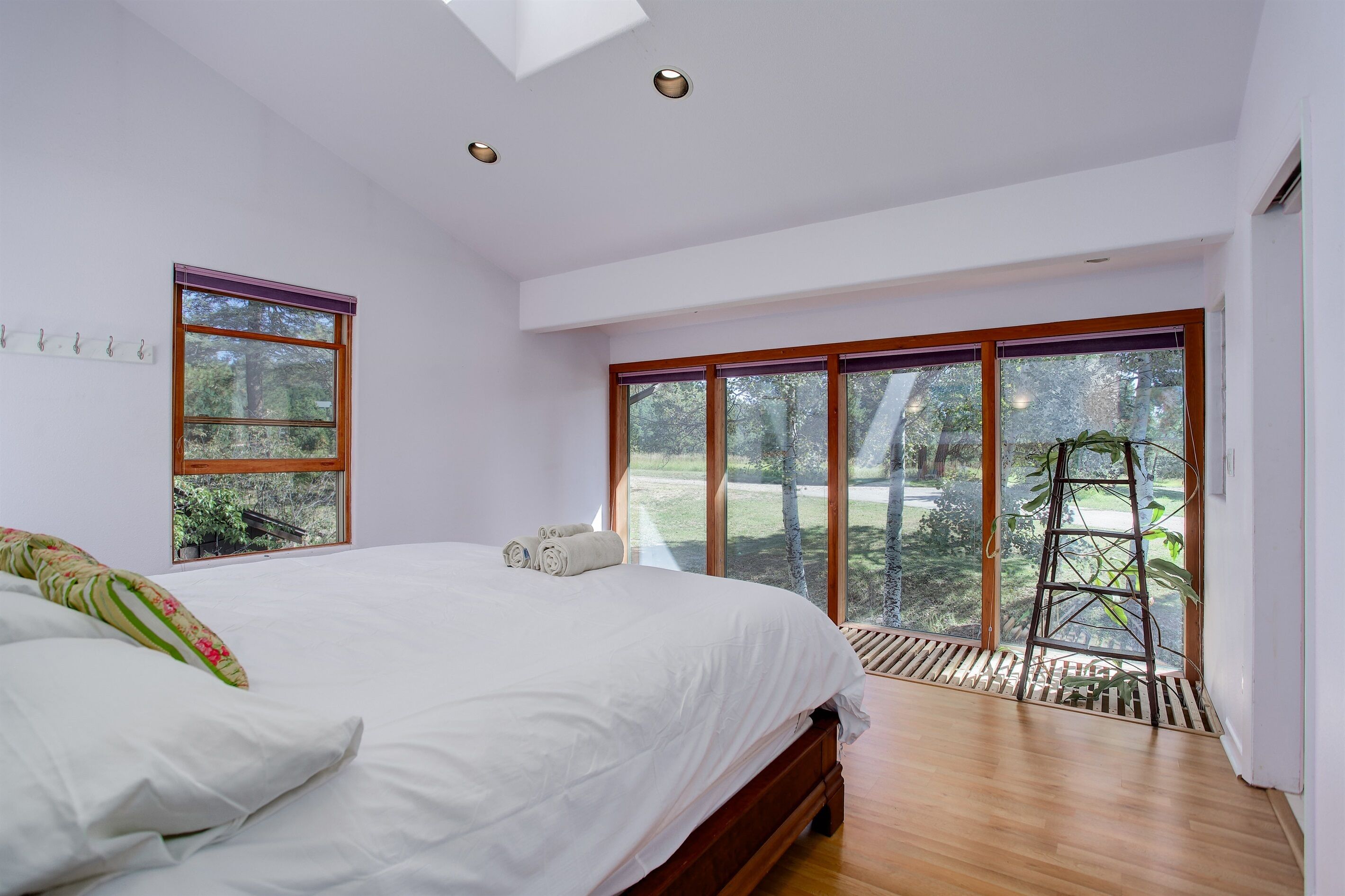 Een slaapkamer met een groot bed, een dakvenster, een raam met uitzicht op bomen en een houten ladder tegen de muur.
