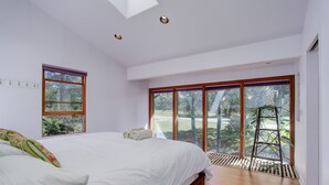 Ein Schlafzimmer mit einem großen Bett, einem Oberlicht, einem Fenster mit Blick auf Bäume und einer an der Wand lehnenden Holzleiter.