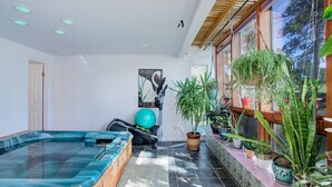Ein moderner Innenraum mit Whirlpool, Fitnessgeräten und verschiedenen Kübelpflanzen.