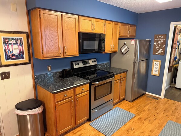 A kitchen with wooden cabinets, a stainless steel refrigerator, a microwave, and a stove. - Celebrate Claire de Lune Mountain Lake Home (Hayesville)