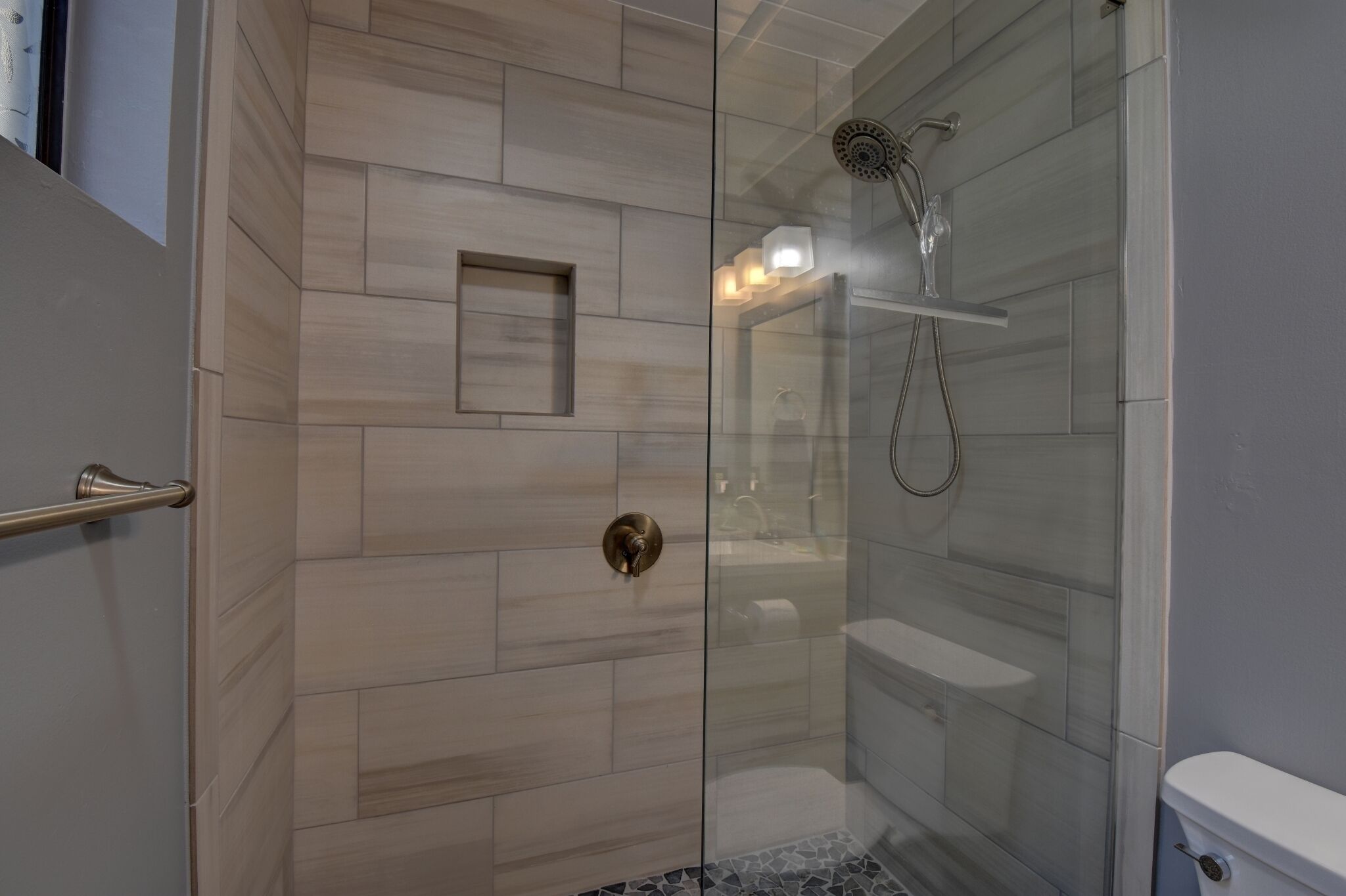 Une douche moderne avec une porte en verre, une petite étagère et un porte-serviettes.