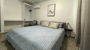 Quarto com cama, poltrona, mesa de cabeceira, ar condicionado e quadro na parede.