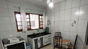 Eine Küche mit weißen Fliesen, einem Gasherd, einem Spülbecken, einem Fenster mit Vorhängen und einem Deckenventilator.