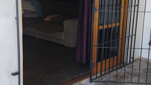 Eine offene Tür, die in einen Raum mit einem Bett, einer Kommode und einem Wandventilator führt.