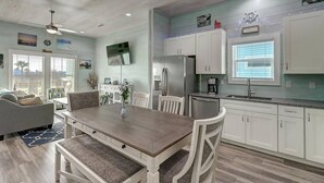 A modern kitchen with white cabinets, stainless steel appliances, and a dining area with a wooden table and chairs. - Paradise on Copano Bay ~ Complementary Kayaks ~ Pier and Pool  (Rockport)