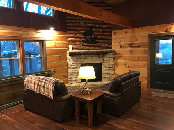 L’intérieur d’un chalet chaleureux, avec une cheminée en pierre, des canapés en cuir et une couverture à carreaux posée sur l’un des canapés.