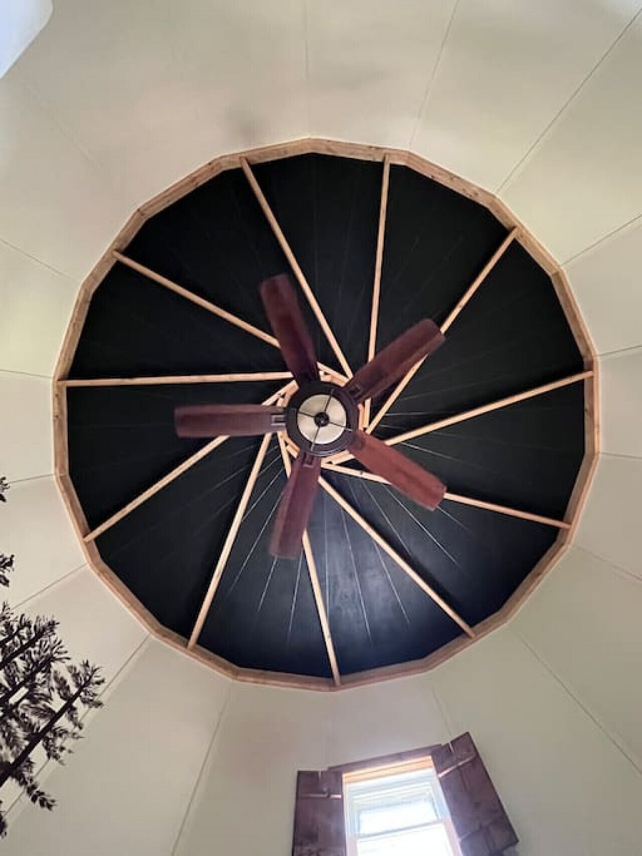 Un escalier en colimaçon avec une structure en bois et des marches noires, menant à un ventilateur de plafond doté de pales en bois.