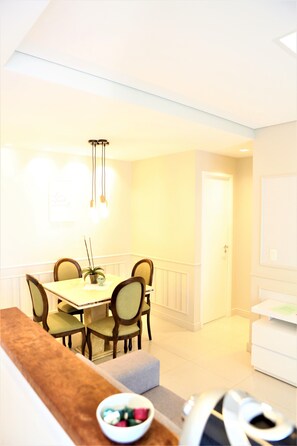 A dining area with a table and chairs, a plant on the table, and a bowl of fruit on the table's edge. - Apartament (Centro Campinas)