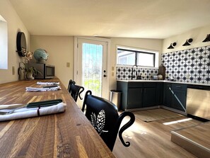 Een eetgedeelte met een houten tafel, stoelen, en een keuken met een spatwand met sterrenpatroon.