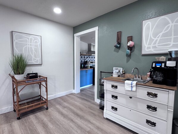 A kitchen with a coffee station, a white cabinet with drawers, and a plant on a cart.