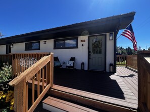 Une terrasse en bois avec une pancarte de bienvenue, une porte ornée d’une guirlande et un drapeau américain.