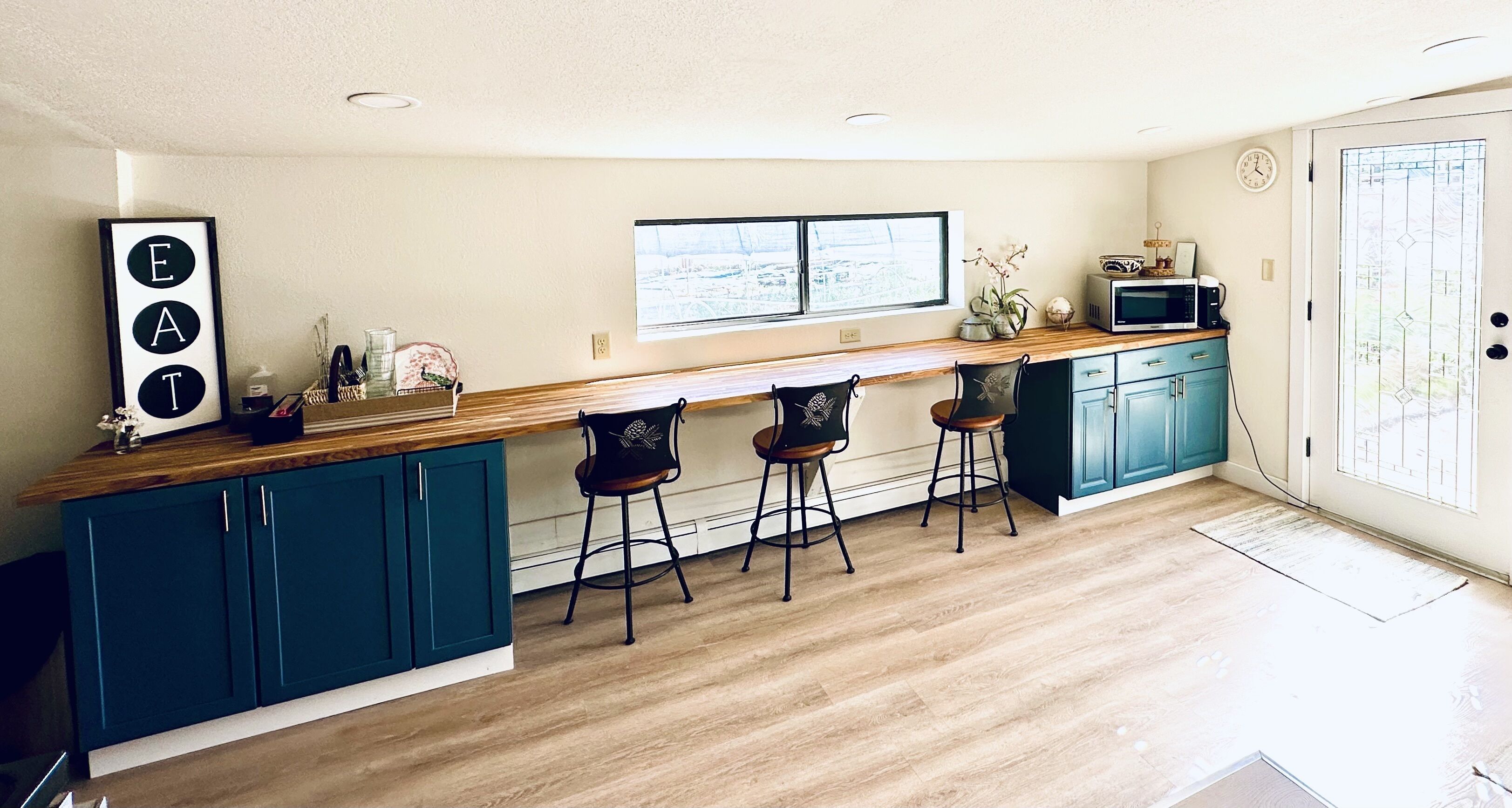 A modern kitchen with teal cabinets, a wooden countertop, and bar stools.