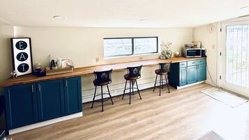 A modern kitchen with teal cabinets, a wooden countertop, and bar stools.