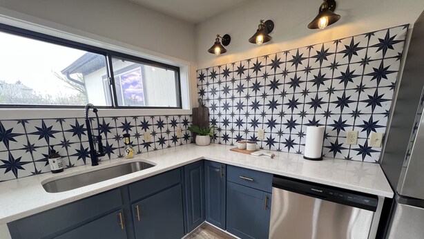 Une cuisine moderne avec des meubles bleu foncé, un lave-vaisselle en acier inoxydable et un pare-feu décoratif.