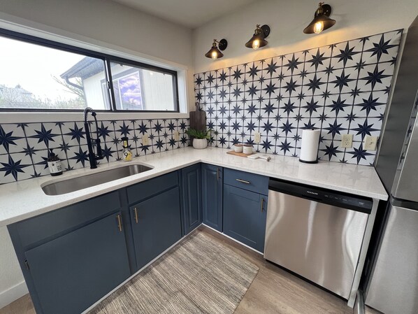 Une cuisine moderne avec des meubles bleu foncé, un lave-vaisselle en acier inoxydable et un pare-feu décoratif.