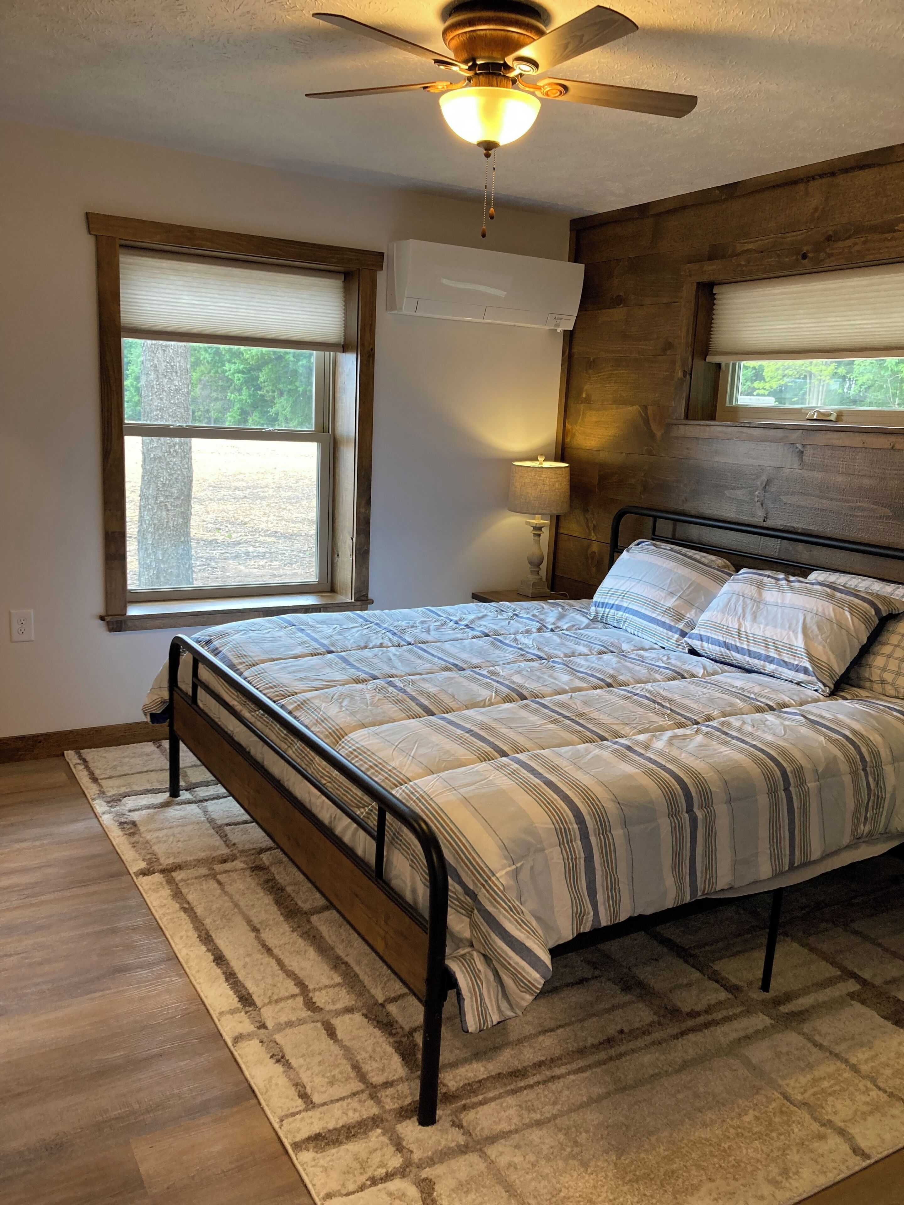 A bedroom with a bed, a ceiling fan, a window with blinds, and a wall-mounted air conditioner.