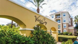 Un arco amarillo con el texto "Vista Cay Resort" y un edificio al fondo.