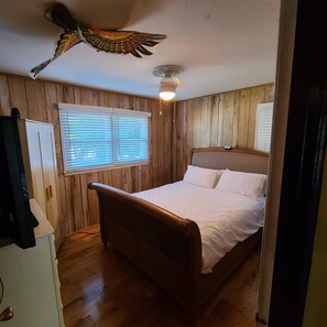 Cozy retreat with a bed, bedside table, and window with blinds, set against a unique bird mural ceiling.
