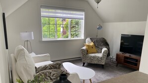 A living room with a white sofa, a patterned armchair, a black vase, and a television on a wooden stand. - Beautiful views, quiet space (Victoria)