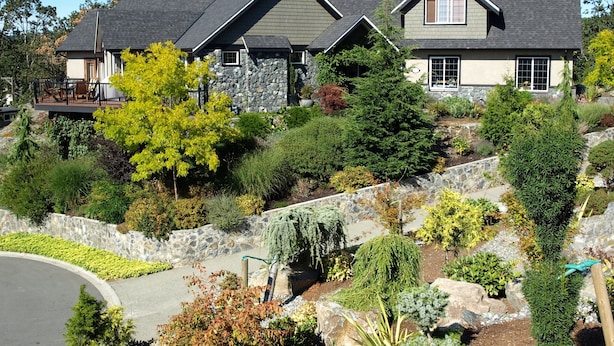 A two-story house with a stone facade, a balcony, and a landscaped garden with various shrubs and trees. - Beautiful views, quiet space (Victoria)