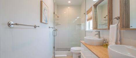 Une salle de bain moderne avec une douche à parois de verre, des toilettes blanches et deux vasques dotées de plans de travail en bois.