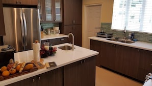 A modern kitchen with dark wood cabinets, stainless steel appliances, a white countertop, and a window with blinds. - The Happy Place- 4BR Beachfront Fully Staffed Villa w/ Eternity Pool (Montego Bay)