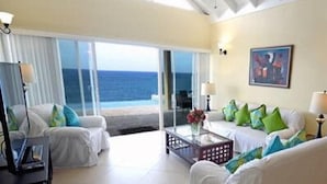 A hotel room with a balcony, white furniture, and a painting on the wall. - The Happy Place- 4BR Beachfront Fully Staffed Villa w/ Eternity Pool (Montego Bay)