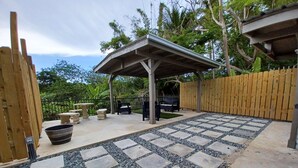 En udendørs patio med stentilfliser, en pergola og et træhegn.