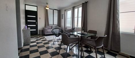 A room with a checkered floor, a dining table with chairs, a sofa, and a ceiling fan.