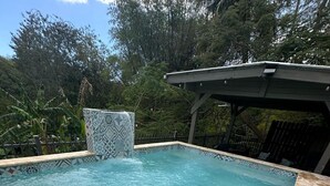 Et rektangulært pool med klart blåt vand, omgivet af en stendækning og en mønstret flisekant.