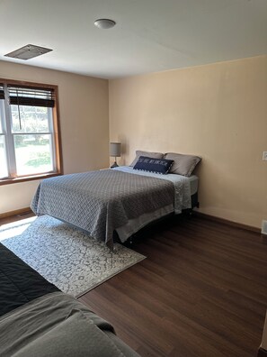 Une chambre à coucher comprenant un lit, une table de chevet, une lampe, une fenêtre avec des stores et un tapis à motifs.