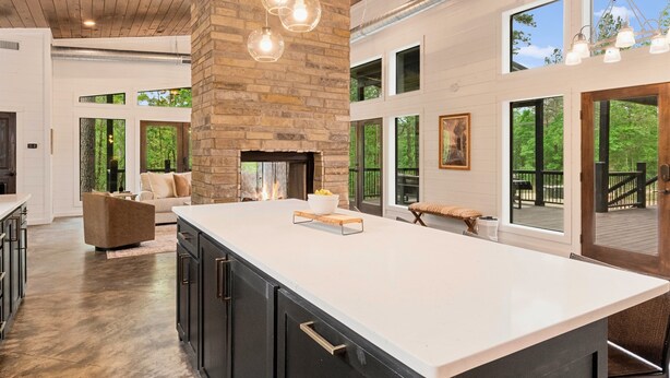 A spacious kitchen with a large island, stone fireplace, and multiple windows offering views of the outdoors. - Luxury Mountain Cabin Retreat in Broken Bow (Broken Bow)