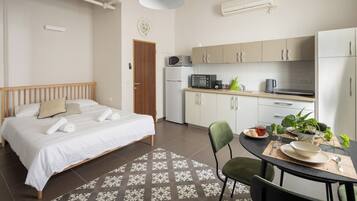 A bedroom with a bed, a dining table with chairs, a kitchen area with appliances, and a small potted plant.