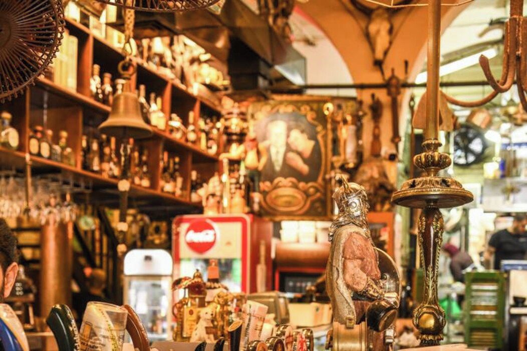 A cluttered shop with various items on shelves and hanging, including a bell and a statue.