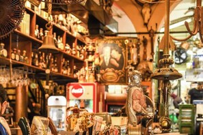 Une boutique encombrée, avec divers objets exposés sur des étagères et suspendus au plafond, notamment une cloche et une statue.