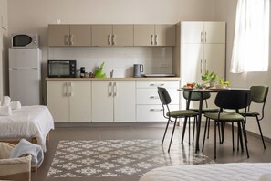 Une chambre d’hôtel avec une kitchenette, un coin repas comprenant quatre chaises, un lit avec du linge de lit blanc et un tapis à motifs.