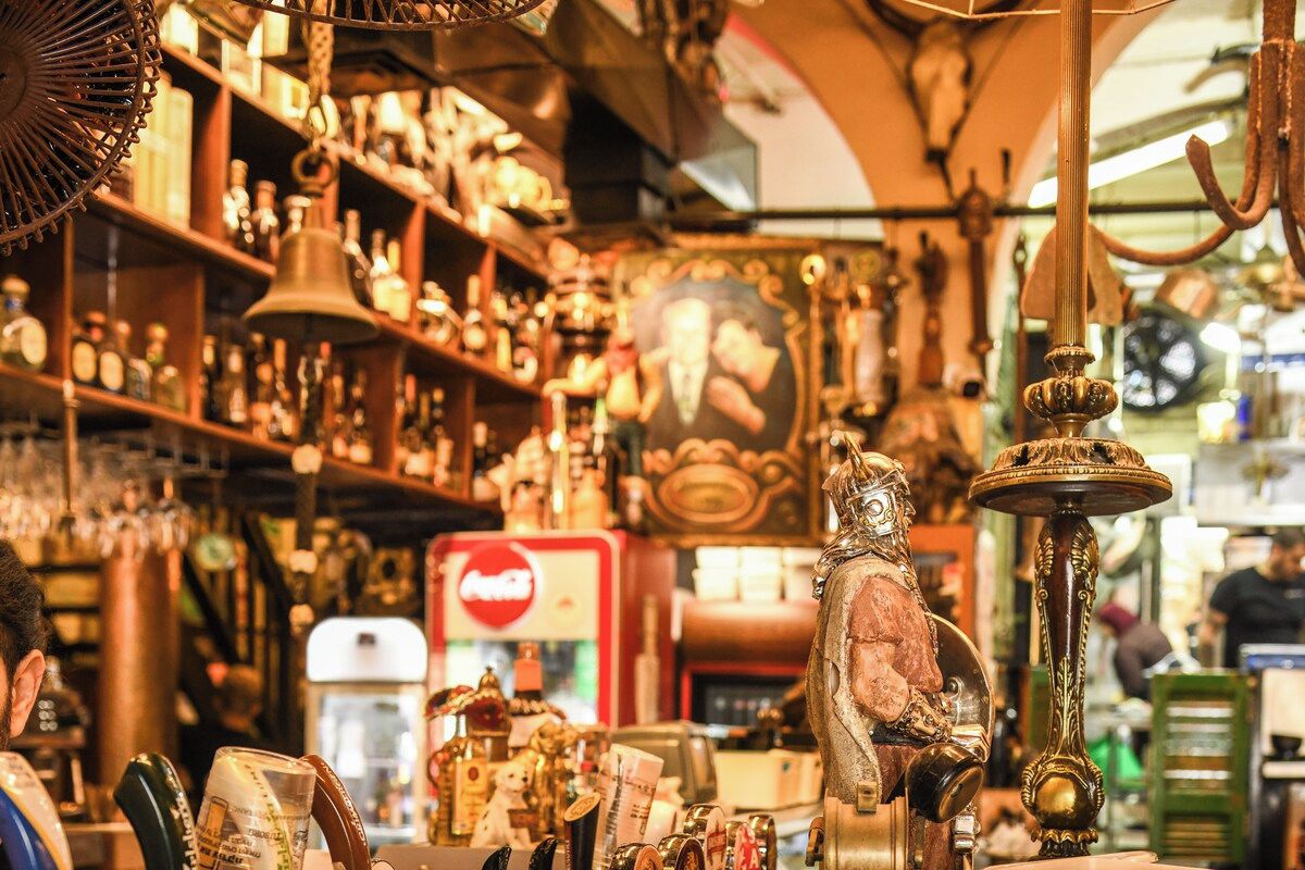 Una tienda de antigüedades desordenada con varios artículos a la vista, incluyendo una campana, una estatua y un refrigerador de Coca-Cola.