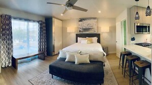 A modern bedroom with a large bed, a bench, a desk, and a kitchenette. - Stunning Ocean Beach Gem - has everything! (San Diego)