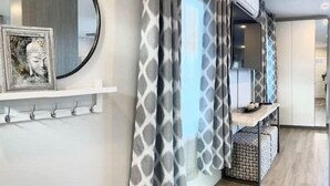 A modern hotel room with a wooden floor, a round mirror, a wall-mounted shelf with a Buddha statue, patterned curtains, and a small seating area with a patterned ottoman. - Stunning Ocean Beach Gem - has everything! (San Diego)