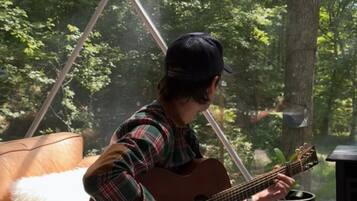 Una persona asseguda en un sofà de cuir tocant la guitarra en una habitació amb un gran finestral que donava a un bosc.