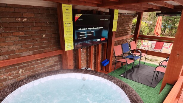 Un espace avec un jacuzzi, doté d’un écran de télévision diffusant un message, et entouré de poutres en bois et de murs en briques.
