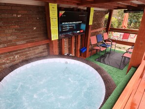 A hot tub area with a TV screen displaying a message, surrounded by wooden beams and brick walls.