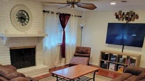 Un salon avec une cheminée, un ventilateur de plafond, un téléviseur à écran plat et une bibliothèque.
