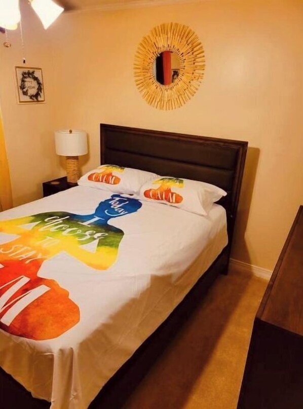 A hotel room with a bed, a nightstand with a lamp, a wall decoration, and a framed picture.