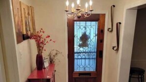 Un couloir doté d’un plancher en bois, d’un lustre, d’un vase contenant des fleurs séchées et d’une porte surmontée d’un portail en métal.