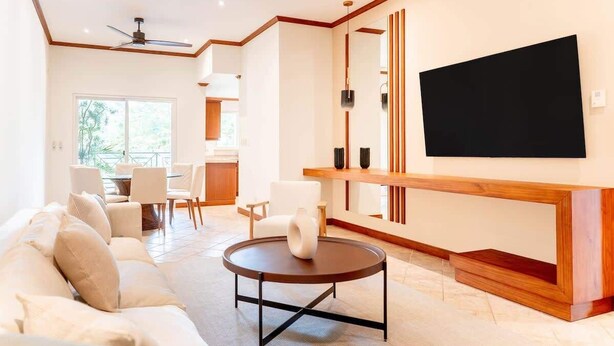 A modern living room with a sofa, a round coffee table, a TV mounted on the wall, and a dining area with chairs and a table. - Stylish Apartment w/ Hotel Amenities @ Los Sueños (Playa Herradura)