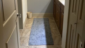 Ein schmaler Flur mit einem Badezimmer rechts, ausgestattet mit einem Waschbecken und Schränken.