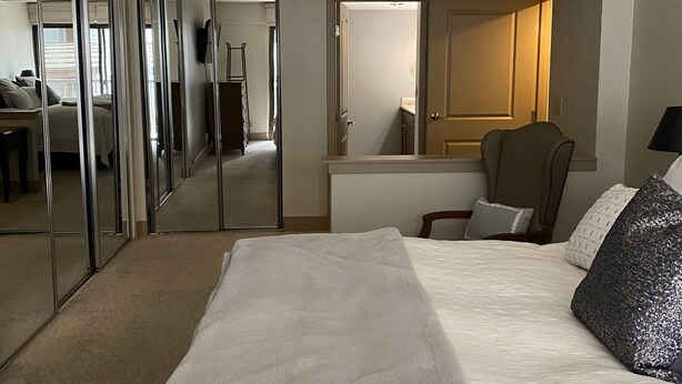 Ein Hotelzimmer mit Bett, Stuhl, Schreibtisch, Spiegel und Kleiderschrank.